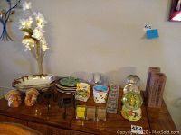 Photo showing assorted decorative plates, two turkey salt and pepper shakers, glass candle holders with candles, a floral arrangement with LED lights, snow globes, and brown textured decorative items placed on a wooden surface.