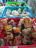Three plastic baskets filled with assorted figurines including bears, children, animals, and flowers, with one white rabbit figurine from Herend.