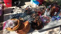 Wide view of table with mixed wire, tin, ceramic, glass flower pots, holders, and baskets, bags of pine cones, and assorted planters.