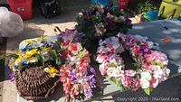 Four professional artificial flower arrangements displayed on a table, featuring a basket arrangement and various wreath styles in multiple colors.