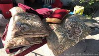 King size comforter with two matching floral damask pillows and velvet throw pillow folded on table outdoors