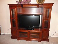 Front view of the wooden entertainment center with central TV space, side glass-door cabinets, and lower glass panel cabinets. Shows color and finish.