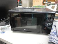 Front view of a black Magic Chef microwave oven showing door, keypad panel, and power cord.