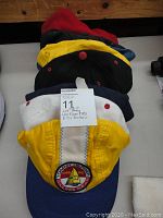 Caps stacked with a visible yellow cap featuring Tommy Hilfiger Sailing Gear logo patch, showing colors white, yellow, blue, black, and red hats.
