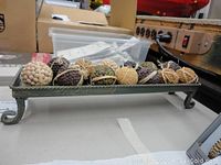 Full view of rectangular metal decorative tray containing 13 assorted seeded decorative balls with various textures and colors.