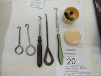 Photo showing six antique shoe button hooks and a closed celluloid box containing shoe buttons