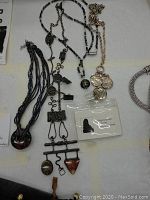 Top down photo showing four pieces of assorted costume jewelry including murano glass necklace, metal lanyard with charms, gold-tone coin pendant necklace, and dark beaded necklace.