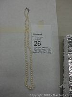Image of a single strand cream colored pearl necklace laid out with auction lot label