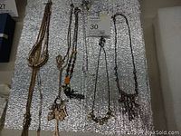 Six assorted costume jewelry necklaces displayed on foam, showing various styles of chains and pendants.