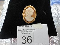 Image of front of cameo pin/necklace showing carved profile and gold filled frame on black background.