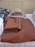 Folded brown sheets, smooth in texture, folded pillowcases on top.