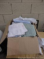Box filled with towels and cloths in white, light blue, green, gray, and pink colors.