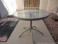 Round glass top patio table on a concrete floor, showing overall condition and design.