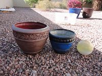 Two fiberglass pots placed on gravel ground with a yellow spherical object beside them for scale in outdoor setting