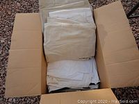 Box containing multiple pairs of men's pants, mostly cream and white colors, folded