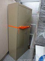 Full view of the beige metal cabinet secured with an orange strap, showing height and width dimensions.