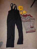 Full lot view showing black Helly Hansen bibs, patterned sweater, yellow gloves, Tommy Hilfiger yellow hat