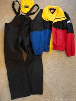 Full view of Tommy Hilfiger ski jacket, Norska quilted bib pants, and yellow fleece hat laid out on carpet.