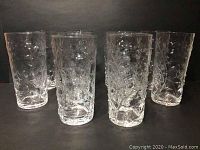 Set of tall clear glass tumblers with embossed floral pattern arranged upright on black background.