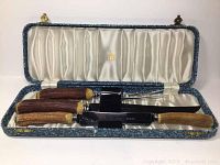 Full view of the carving set inside original blue textured case with satin lining showing the knife and fork handles made of stag horn and Bakelite.
