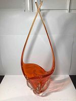 Front view of tall orange blown glass centrepiece bowl with chalet-style design and curved elongated handles forming a crossed top