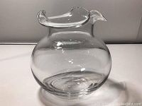 Clear glass vase with rounded body and ruffle top edge, photographed on white background exhibiting transparency and shape details.
