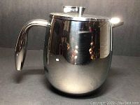 Side view of polished stainless steel French press coffee maker with handle and lid