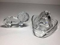 Both paperweights side by side showing lion and cowboy hat shape in clear solid glass.