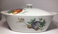 Side view of the oval white ceramic covered vegetable dish showing colorful pear and root vegetable design on the side