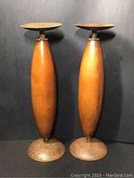 Front view of two wooden candle holders with bronze plates and bases against a black background.