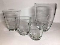 Four nesting clear crystal vases with etched sailboat designs arranged standing separately