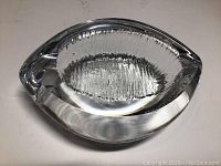 Clear oval-shaped Daum crystal ashtray with textured vertical pattern inside and smooth polished outside, shown from above angle.