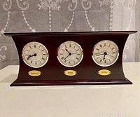 Front view showing all three clock faces with city name plaques below each: Vancouver on left, Chicago center, Toronto right. Wood case has dark polished finish.