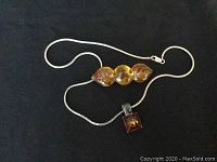 Sterling silver necklace and amber brooch laid out on a dark surface.