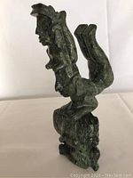 Full side view of the green stone figurine depicting intertwined human figures carved in detail