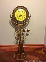Full view of the vintage battery clock on metal stand approximately 28 inches tall, showing decorative metal floral and leaf accents.