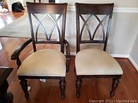 Two dining chairs including one captain's chair with arms and one armless chair, showing dark wood frames and taupe cushioned seats on wood flooring.
