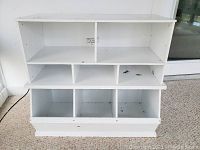 Front view of the white cubby storage unit showing multiple cubby compartments and general wear including marks and stains.