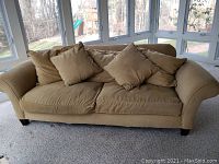 Front view of camel colored fabric sofa with five cushions in a bright room with large windows.