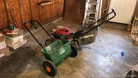 Overview of Honda mower parked next to green Scotts spreader in garage