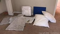 Multiple white pillows laid on carpet, two small rugs/mats nearby, and packaged duvet visible in background