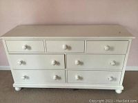 Front view of the white wooden dresser with 7 drawers and round wooden knobs, showing overall condition and design.