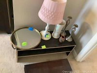 Photo showing wood lamp with pink shade, round mirror with rope hanger, Beleek vase, smaller multicolor vase, and pair of matte nickel candlesticks on top of floating wood shelves