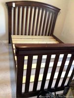 Full view of the dark wood slatted bed frame showing footboard and headboard at an angle with slats assembled and rails visible.