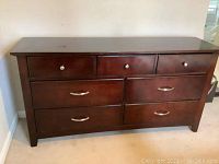 Front view of dark wood dresser with 7 drawers and metal handles showing overall condition and color.