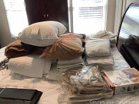 Stack of linens, pillows, packaged blackout curtain liners, and other items on surface