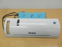 Top front view of the white Scotch laminator showing the brand name, manual knob, and laminated usage instructions attached on top.