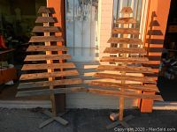 Two wooden Christmas trees standing outdoors against a building wall in natural light.