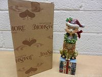 Photo showing the cat figurine with Santa hat and wreath on a decorated block next to the Jim Shore branded box.