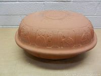 Full side view of the terra cotta oven showing embossed classical figures and columns on the lid and base.